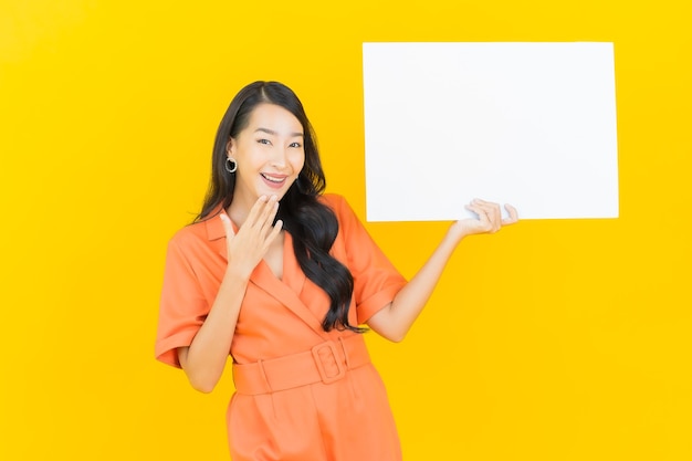 Retrato hermosa mujer asiática joven sonrisa con cartelera blanca vacía en amarillo