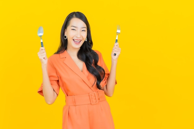 Retrato hermosa mujer asiática joven sonrisa con cuchara y tenedor en amarillo