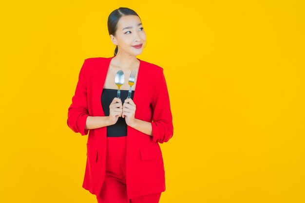 Retrato hermosa mujer asiática joven sonrisa con cuchara y tenedor en amarillo