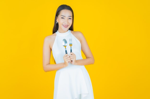 Retrato hermosa mujer asiática joven sonrisa con cuchara y tenedor en amarillo
