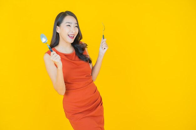 Retrato hermosa mujer asiática joven sonrisa con cuchara y tenedor en amarillo