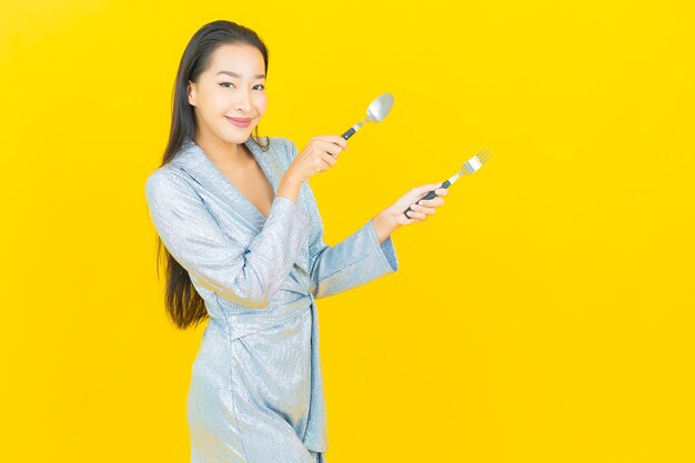 Retrato hermosa mujer asiática joven sonrisa con cuchara y tenedor en la pared amarilla