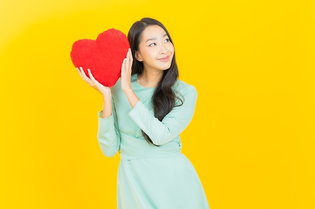 Retrato hermosa mujer asiática joven sonrisa con forma de almohada de corazón en amarillo