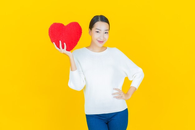 Retrato hermosa mujer asiática joven sonrisa con forma de almohada de corazón en amarillo