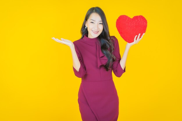 Retrato hermosa mujer asiática joven sonrisa con forma de almohada de corazón en amarillo