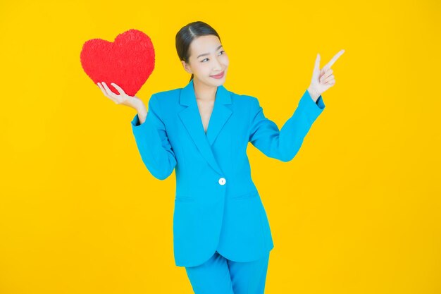 Retrato hermosa mujer asiática joven sonrisa con forma de almohada de corazón en amarillo