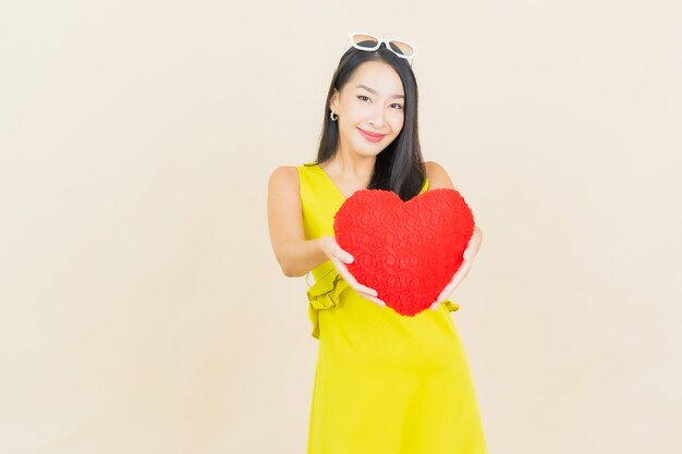 Retrato hermosa mujer asiática joven sonrisa con forma de almohada de corazón en la pared de color