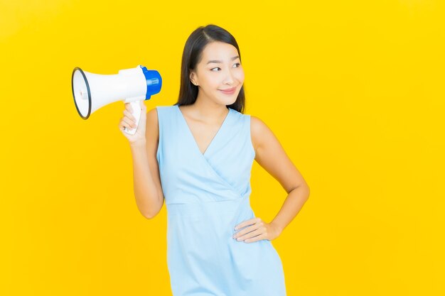 Retrato hermosa mujer asiática joven sonrisa con megáfono en la pared de color amarillo