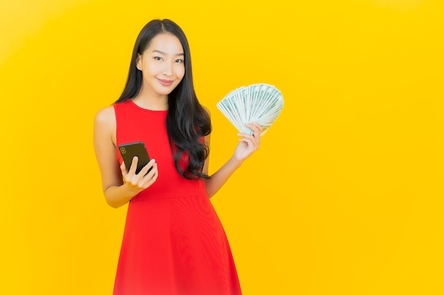 Retrato hermosa mujer asiática joven sonrisa con mucho dinero en efectivo y dinero en la pared amarilla