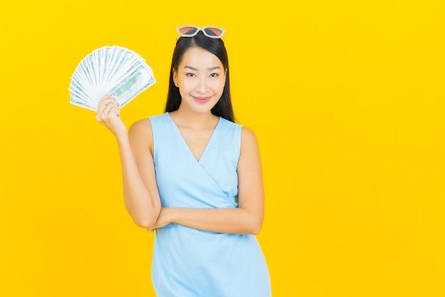 Retrato hermosa mujer asiática joven sonrisa con mucho dinero en efectivo y dinero en la pared de color amarillo