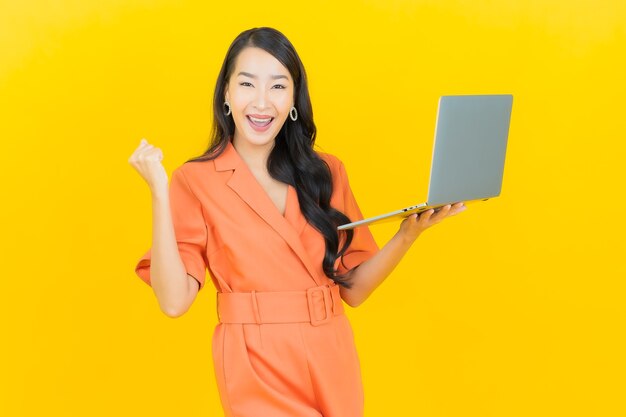 Retrato hermosa mujer asiática joven sonrisa con ordenador portátil en amarillo