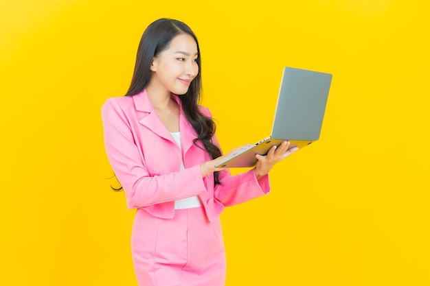 Retrato hermosa mujer asiática joven sonrisa con ordenador portátil en la pared amarilla aislada