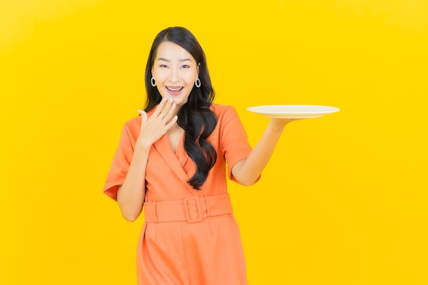 Retrato hermosa mujer asiática joven sonrisa con plato plato vacío en amarillo