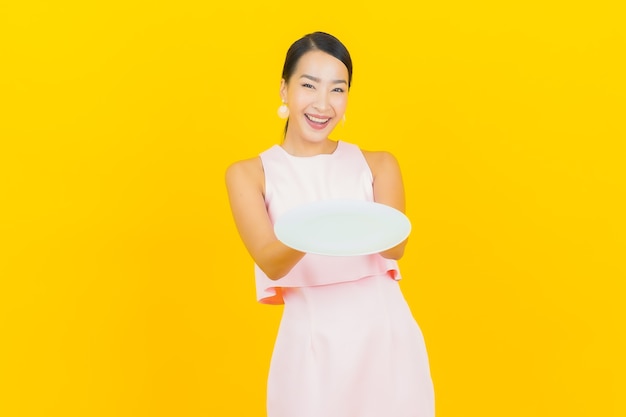 Retrato hermosa mujer asiática joven sonrisa con plato plato vacío en amarillo