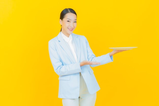 Retrato hermosa mujer asiática joven sonrisa con plato plato vacío en amarillo