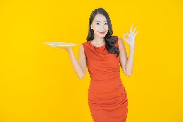 Retrato hermosa mujer asiática joven sonrisa con plato plato vacío en amarillo