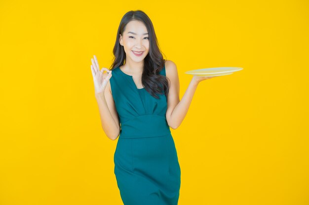 Retrato hermosa mujer asiática joven sonrisa con plato plato vacío en amarillo