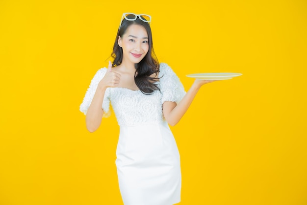 Retrato hermosa mujer asiática joven sonrisa con plato plato vacío en amarillo