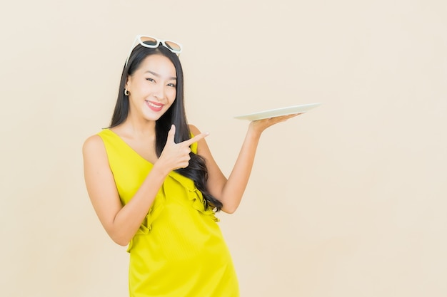 Retrato hermosa mujer asiática joven sonrisa con plato plato vacío en la pared de color