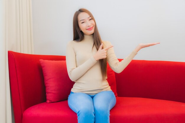 Retrato de hermosa mujer asiática joven sonrisa relajarse en el sofá en el interior de la sala de estar