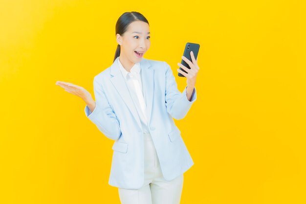 Retrato hermosa mujer asiática joven sonrisa con teléfono móvil inteligente en amarillo