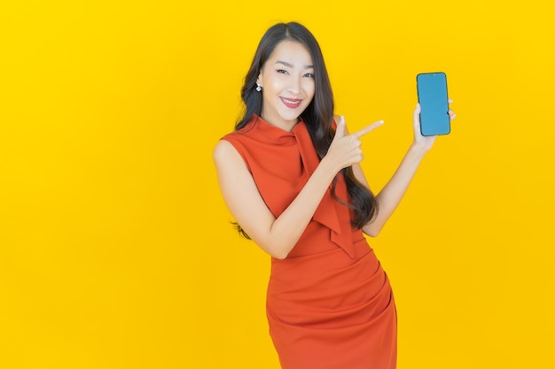 Retrato hermosa mujer asiática joven sonrisa con teléfono móvil inteligente en amarillo