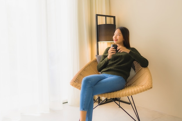 Retrato hermosa mujer asiática joven sostenga la taza de café y sentado en el sillón