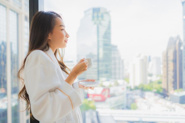 Retrato hermosa mujer asiática joven sostenga la taza de café con vistas a la ciudad
