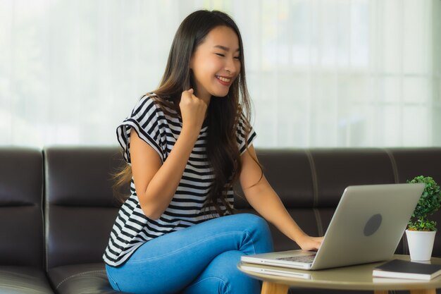 Retrato de hermosa mujer asiática joven usando laptop en el sofá