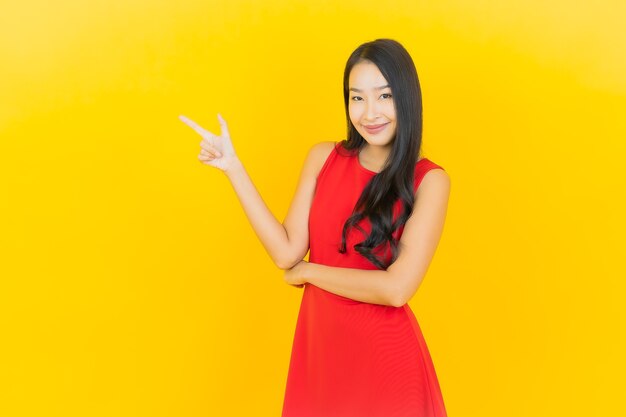 Retrato hermosa mujer asiática joven usar vestido rojo sonrisa con acción en la pared amarilla