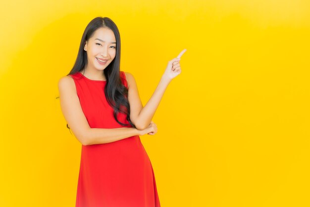 Retrato hermosa mujer asiática joven usar vestido rojo sonrisa con acción en la pared amarilla