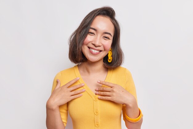 Retrato de hermosa mujer asiática sincera con cabello oscuro inclina la cabeza se siente feliz se siente contento usa un puente amarillo aislado sobre una pared blanca