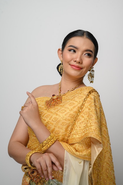 Retrato hermosa mujer asiática en traje de vestido tradicional tailandés sonríe y posa con gracia en la pared blanca