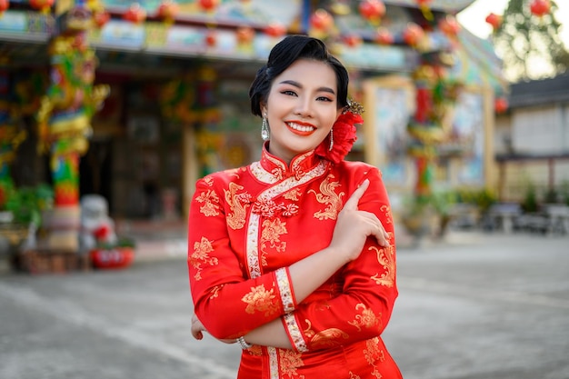 Retrato de hermosa mujer asiática vistiendo un cheongsam sonriendo y posa con gesto de felicitación en el santuario por el año nuevo chino