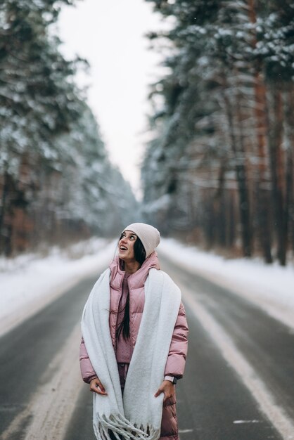 Retrato de una hermosa mujer caucásica en una carretera a través del bosque nevado