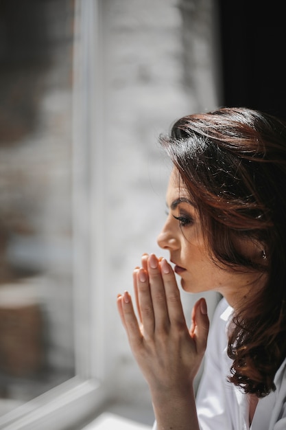 Foto gratuita retrato de hermosa mujer caucásica rezando junto a la ventana en un día soleado.