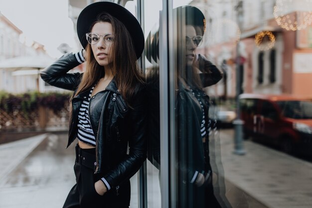 Retrato de una hermosa mujer en la ciudad después de la lluvia cerca de brillantes escaparates en clima frío en el día