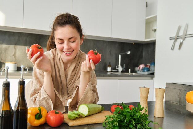 Retrato de una hermosa mujer cocinando en la cocina cortando verduras a bordo sosteniendo tomates