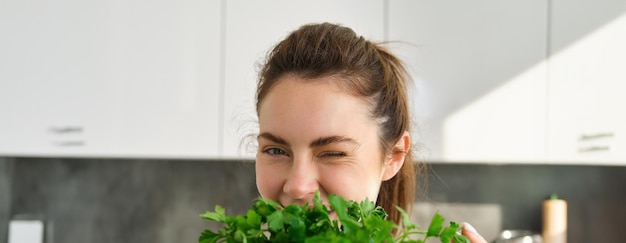 Foto gratuita retrato de una hermosa mujer cocinando sosteniendo perejil fresco agregando hierbas mientras hace que la ensalada sea saludable