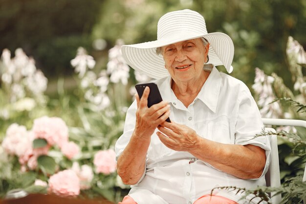 Retrato de hermosa mujer de edad en el parque. Abuela con sombrero blanco. Mujer mayor con teléfono móvil.