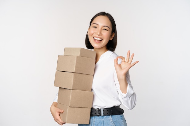 Foto gratuita retrato de hermosa mujer feliz llevar cajas con pedidos empresaria con entrega de acarreo y mostrando bien signo fondo blanco