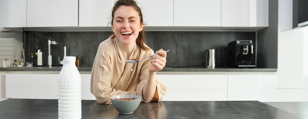 Retrato de una hermosa mujer joven y saludable en bata de baño desayuna en la cocina tiene cereales