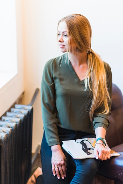 Retrato de hermosa mujer joven sosteniendo revista en la mano mirando forma