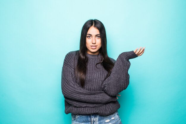 Retrato de una hermosa mujer joven en suéter con la palma abierta aislada en azul