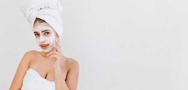 Retrato de hermosa mujer joven con toallas después de tomar el baño hacer mascarilla cosmética en su rostro.