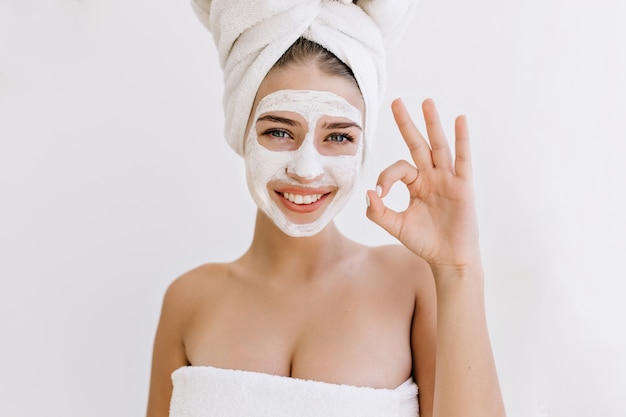 Retrato de hermosa mujer joven con toallas después de tomar el baño hacer mascarilla cosmética en su rostro.