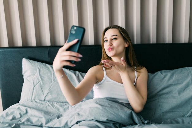 Retrato de hermosa mujer joven tomando un selfie en la cama