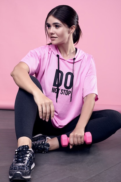 Retrato de una hermosa mujer latina positiva del cuerpo en una sudadera deportiva rosa con ejercicio con pesas en rosa