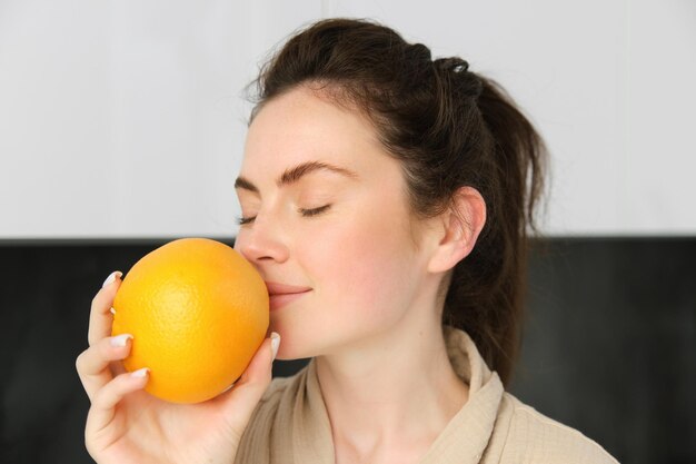 Retrato de una hermosa mujer morena en bata de baño posando con naranja preparando jugo fresco