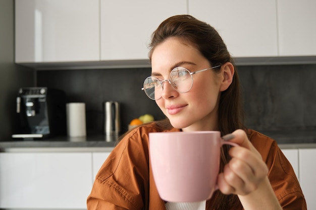 Foto gratuita retrato de una hermosa mujer morena sentada en la cocina tomando un descanso para tomar una taza de café